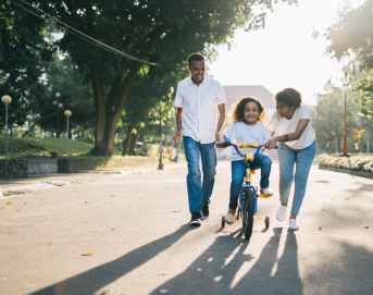 man standing beside his wife teaching their child how to ride bicycle