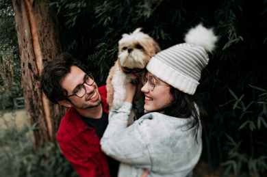 woman lifting puppy in front of man near tree