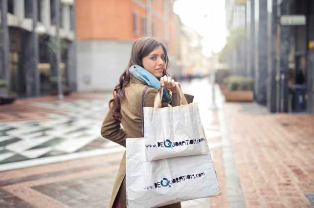 woman in brown coat carrying two white tote bags