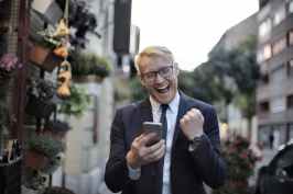 happy businessman checking message on smartphone in downtown alley